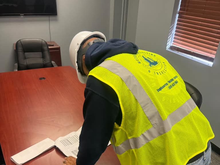 Metric inspector in a branded vest studying drawings on the conference table