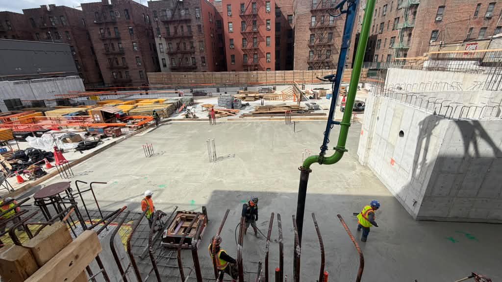 Crew finishing a concrete slab with the pump hose while an inspector watches