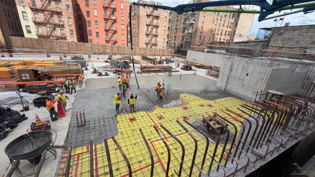 Concrete being pumped onto a reinforced foundation slab between brick buildings in New York City