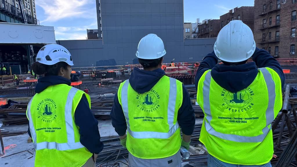 Three Metric inspectors in branded safety vests on a construction site in New York City